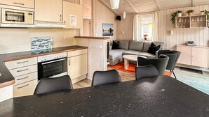 Cocina compacta con estufa, microondas y armarios. Hay una zona de comedor con mesa y sillas, además de una sala de estar con sofá y televisor.