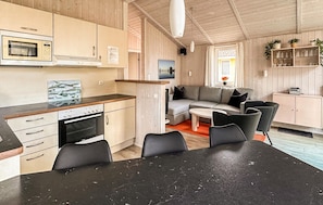 Una cucina compatta con fornello, forno a microonde e mobili. C'è una zona pranzo con tavolo e sedie, e un soggiorno con divano e televisore.