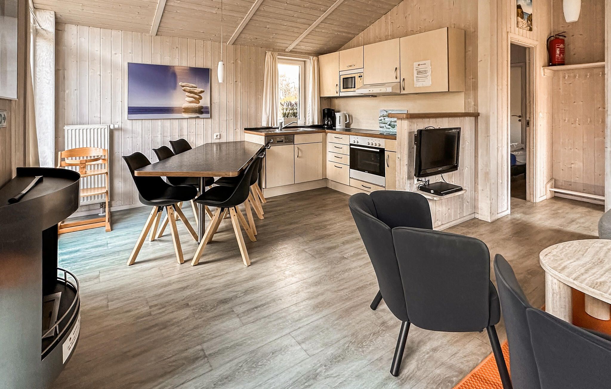 A modern kitchen with a dining area, wooden flooring, and a painting on the wall.