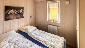 Una habitación con dos camas, una ventana con una planta y un estante en la pared con libros.