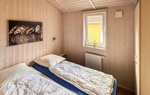 Una stanza con due letti, una finestra con una pianta e una mensola a muro con dei libri.