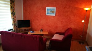 Un salon avec un canapé rouge, une petite table sur laquelle se trouve une télécommande, un téléviseur et une lampe.
