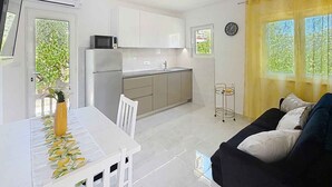 A compact kitchen with white cabinets, a microwave, and a sink. There's a dining table with chairs and a black sofa with cushions. - Holiday apartment in a quiet and sunny location (Baška)