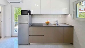 A modern kitchen with white cabinets, a built-in microwave, a stainless steel sink, and a bowl of fruit on the countertop. - Holiday apartment in a quiet and sunny location (Baška)