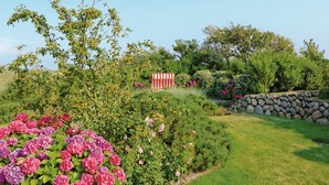 A garden with various plants and flowers, a stone wall, and a red and white striped structure. - House to the lighthouse by A&M - House to the lighthouse (Kampen (Sylt))