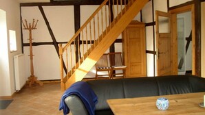 Een kamer met een houten trap, een zwarte leren bank, een houten tafel met een decoratieve vaas en een houten stoel.