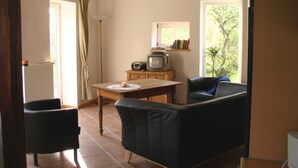 Een woonkamer met een bank, twee fauteuils, een salontafel, een televisie en een raam met uitzicht op groen.