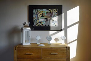 A wooden dresser with drawers, a framed artwork above it, and decorative shells on the dresser.