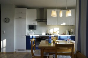 A modern kitchen with white and blue cabinets, a microwave, stove, and a dining table with chairs.