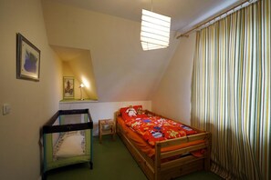 A child's room with a bunk bed, a small table, a crib, and a window with curtains.