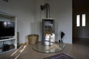 A modern living room with a glass-top coffee table, a television on a white shelf, a fireplace with a chimney, and a wicker basket.