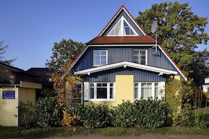 A two-story house with a gabled roof, a satellite dish, and a small garden area.