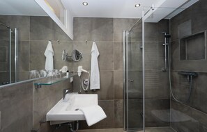 A modern bathroom with a glass shower enclosure, a sink with a mirror, and a glass shelf with toiletries.