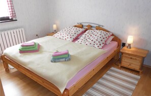 Ein hölzernes Bett mit einer weiß-rosa Bettdecke, zwei Kissen mit einem Blumenmuster und ein Nachttisch mit einer Lampe.