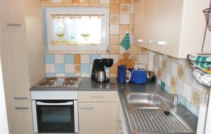 Eine kleine Küche mit Herd, Backofen, Spüle und einem Fenster mit Blumenmuster.
