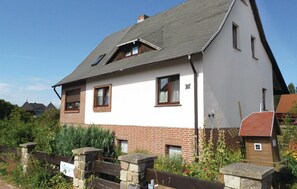 Ein zweigeschossiges Haus mit geneigtem Dach, rotem Klinkermauerwerk im unteren Bereich und weiß verputzter Obergeschoss.