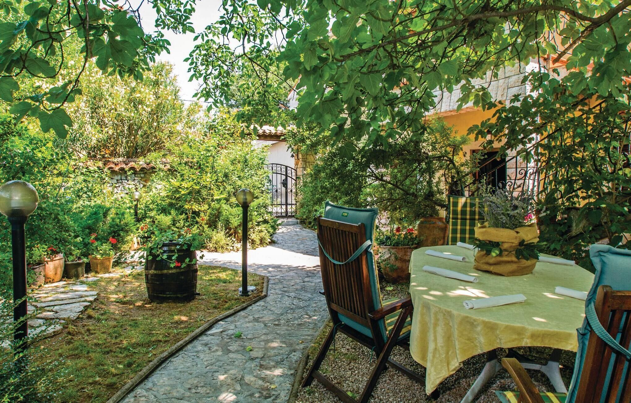 Eine Terrasse im Freien mit Steinplattenboden, einem Tisch mit gelber Tischdecke und Stühlen.