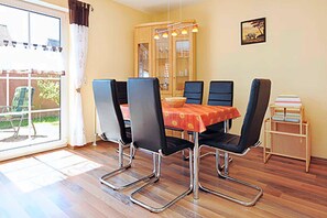 Uma sala de jantar com uma mesa posta para quatro pessoas, cercada por quatro cadeiras, um armário com portas de vidro e uma pequena estante com livros.
