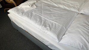 A neatly made bed with white linens and two towels folded on top, a small table with a vase of flowers, and two chairs with cushions. - FW Muschel - House Seewind Warnemünde - Object 25830 (Rostock)