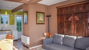 Un salon avec un canapé gris, un fauteuil en osier, un radiateur, un tableau et un meuble en bois.