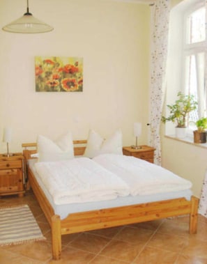 Een slaapkamer met een houten bed, een nachtkastje, een lamp, een schilderij en een raam met gordijnen.
