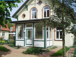 Een woonhuis met twee verdiepingen, een balkon, een voordeur en een klein voortuintje.