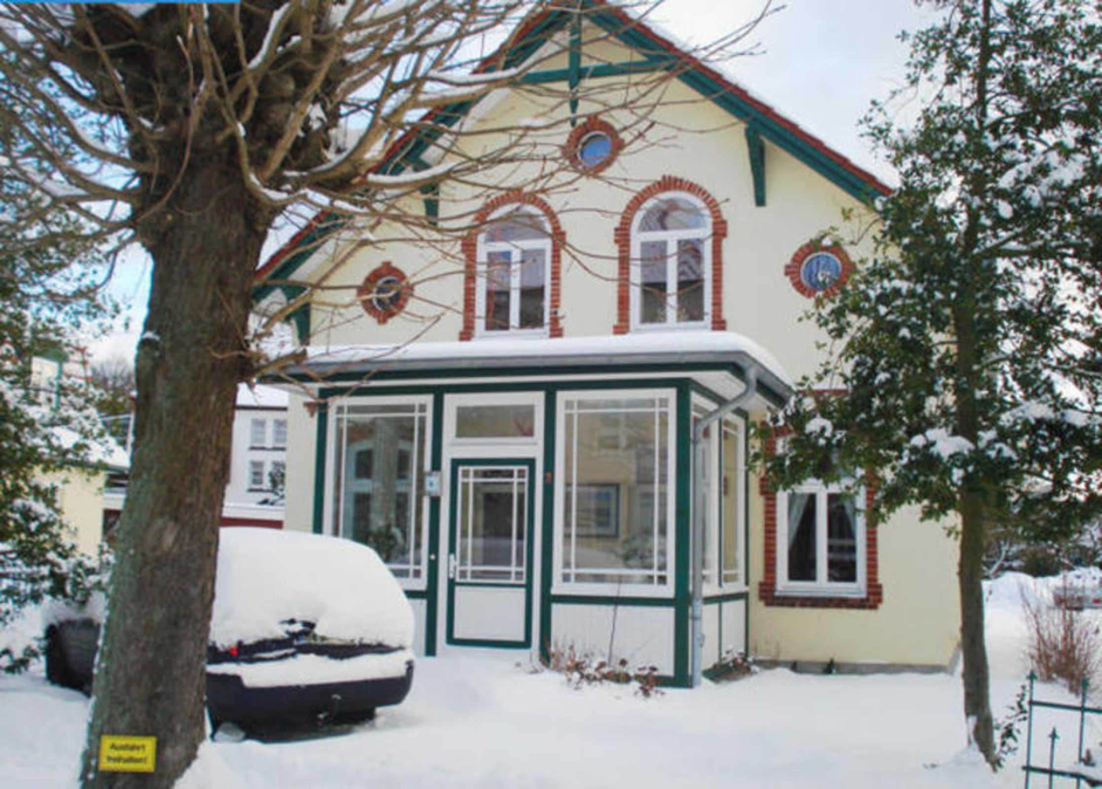 A snow-covered house with a bay window, a garage, and a tree in the foreground.