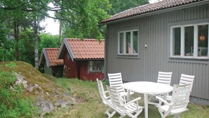 A small, single-story building with a grey exterior and a red-tiled roof. In front of the building, there is a round table with white chairs. - 3 bedroom beautiful home in Trosa (Trosa)