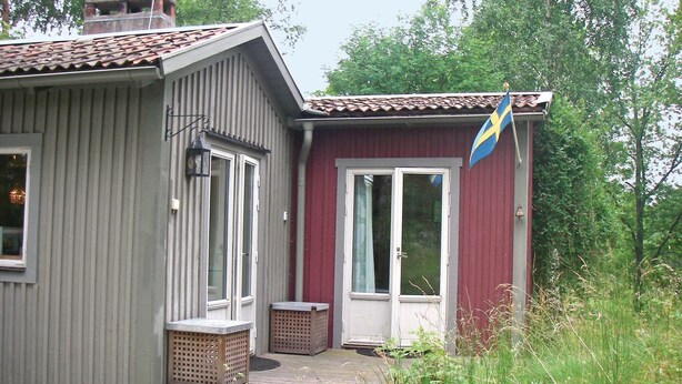 A small house with a red exterior, a white door, and a blue flag on the right. - 3 bedroom beautiful home in Trosa (Trosa)