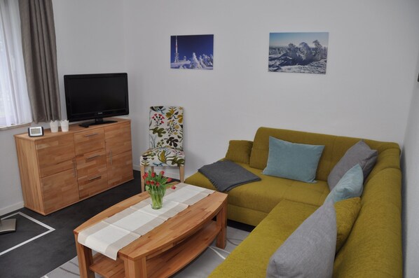 A living room with a sofa, a wooden coffee table, a TV on a cabinet, and two wall-mounted pictures.