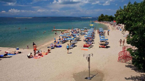 Une plage bordée de rangées de parasols et de chaises longues, une tour de surveillance pour les sauveteurs, et une vue dégagée sur la mer.