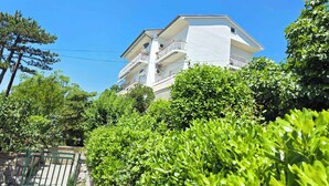 Un immeuble à plusieurs étages doté de balcons, entouré d’une végétation luxuriante.