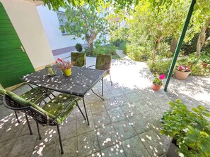 An outdoor patio with a table and chairs, surrounded by potted plants and greenery.