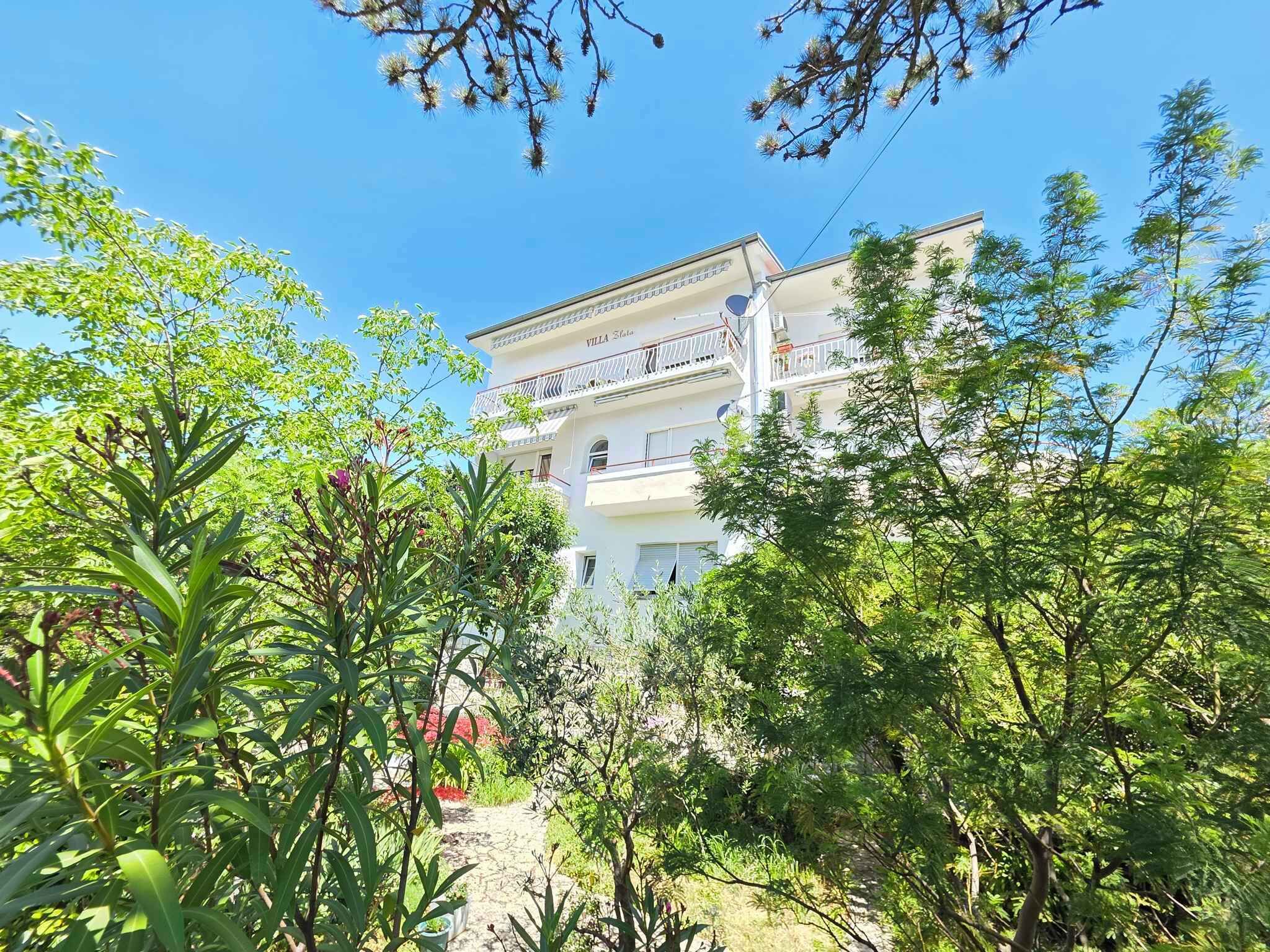 A multi-story building with balconies, surrounded by lush greenery and trees.