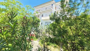 Un immeuble à plusieurs étages doté de balcons, entouré d’une végétation luxuriante et d’arbres.