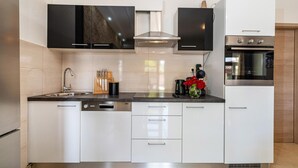 A modern kitchen with white cabinets, a stainless steel range hood, a built-in oven, and a dishwasher. - Stunning home in Radasinovci (Radasinovci)