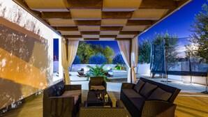 An outdoor seating area with wicker furniture, a table with drinks, and a view of trees and a pool. - Stunning home in Radasinovci (Radasinovci)