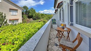 Ein Balkon mit Steinboden, einem Tisch mit Stühlen und Blick auf einen Garten sowie benachbarte Gebäude.