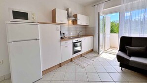 Eine moderne Küche mit weißen Schränken, einem eingebauten Backofen und einer Mikrowelle. Eine Schiebetür aus Glas führt zu einem Balkon mit Blick auf Grünflächen.