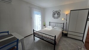 Una camera da letto con un letto, una sedia, una scrivania, una lampada e un armadio.