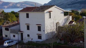 Un edificio bianco su due piani con tetto in tegole rosse, un piccolo balcone e vista su un lago e montagne sullo sfondo.