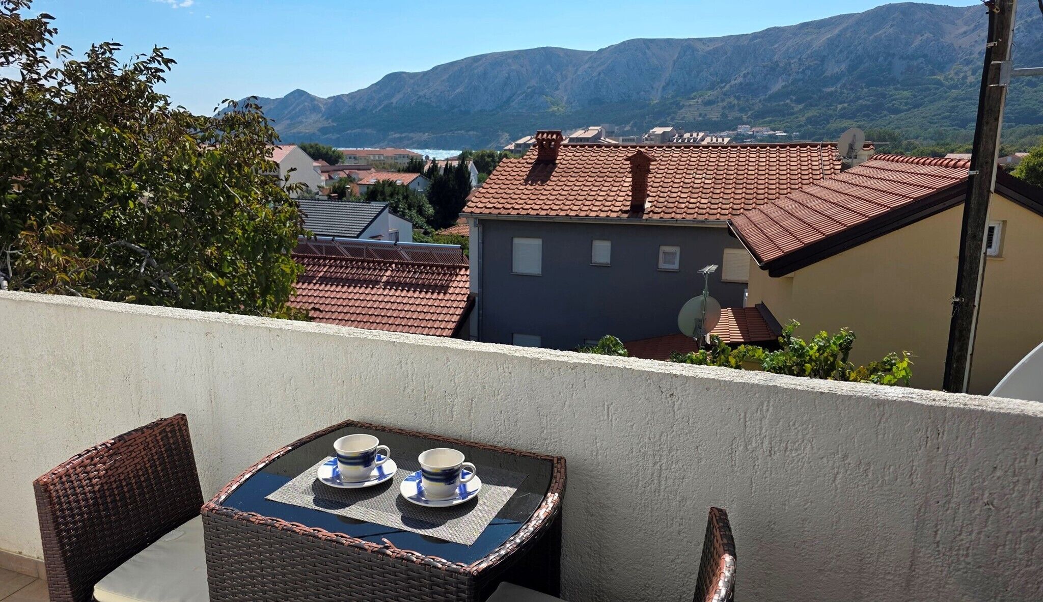 A balcony with a table and chairs, overlooking a mountainous landscape and a village.