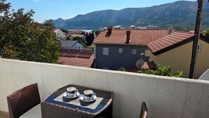 Un balcone con tavolo e sedie, affaccia su un paesaggio montuoso e un villaggio.
