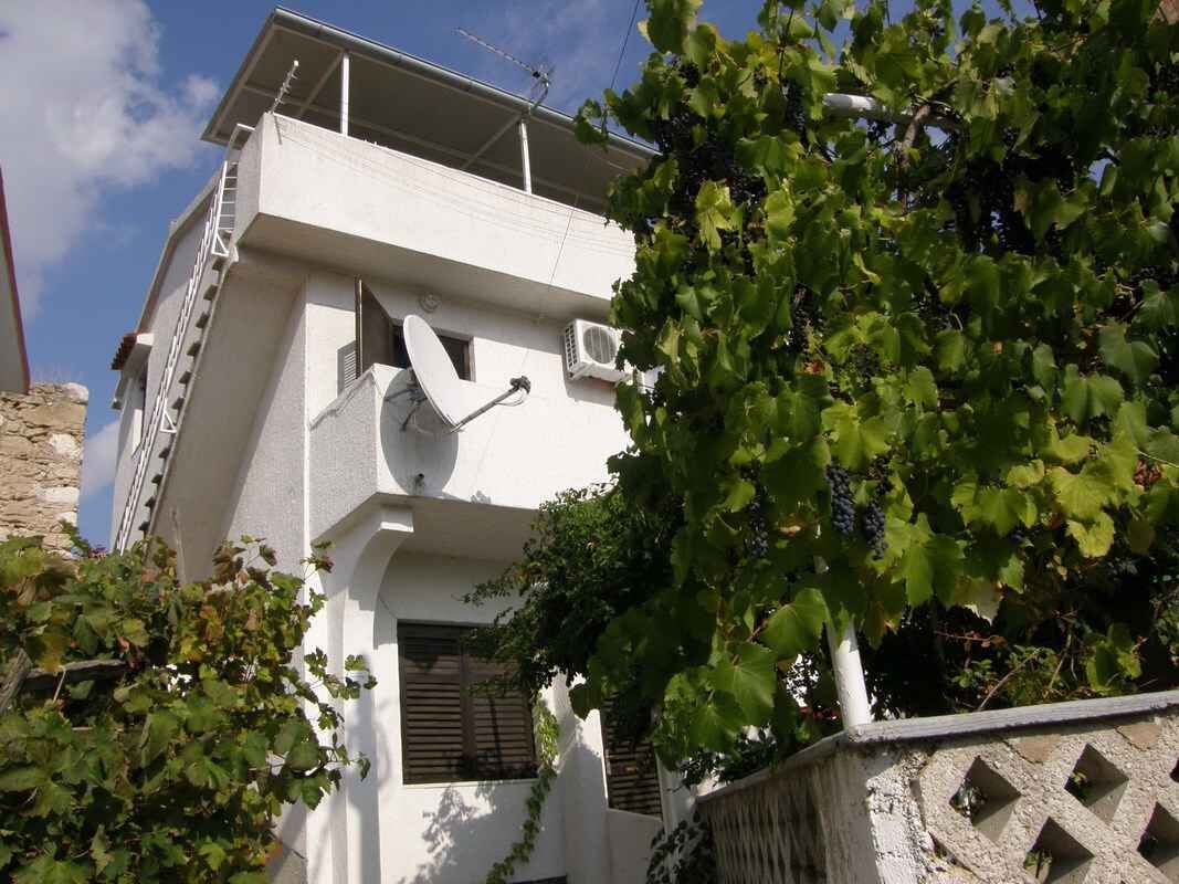 A white building with a satellite dish, a ladder, and a window with shutters.