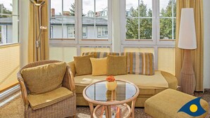 Une pièce comprenant un canapé, des fauteuils, une table en verre et de grandes fenêtres avec des rideaux.