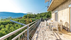 A balcony with a stone floor, white chairs, and a table.