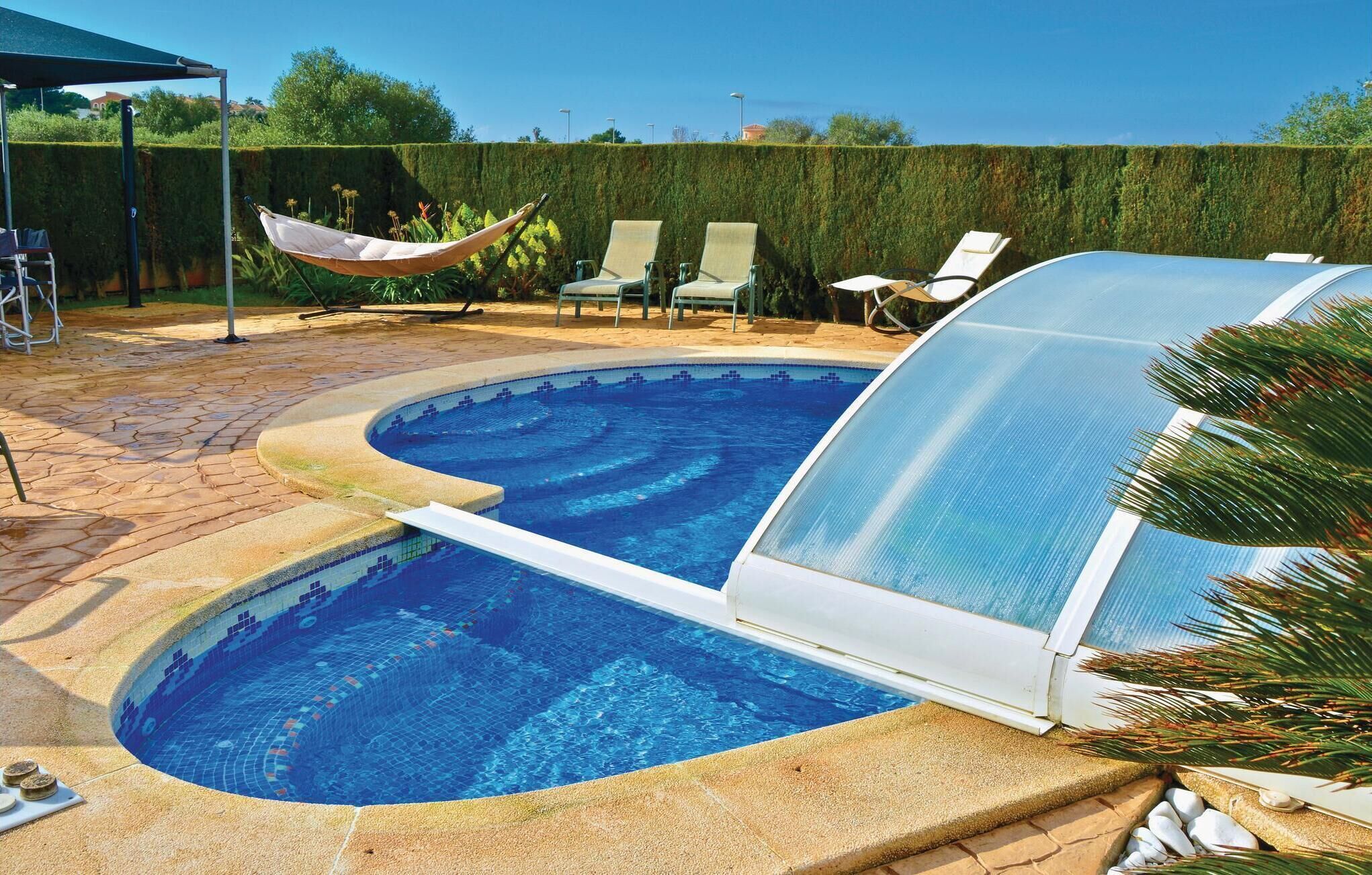 A swimming pool with a glass enclosure, surrounded by lounge chairs and a hammock.