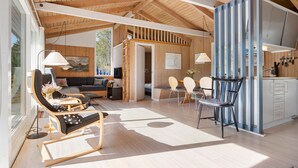 Un salón amplio con techo de madera, un sofá, una mesa de comedor con sillas y una zona de cocina con armarios y un lavabo.