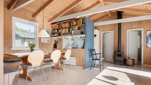 Interior acogedor de una cabaña con comedor de madera, una estantería y un estufa de leña.