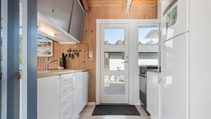 Una cocina pequeña con paredes de madera, una puerta blanca y un refrigerador.